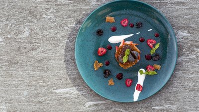 Dessert artistico con frutti di bosco, cioccolato e menta su piatto blu