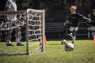 Bambino si allena a calcio con allenatore sull'erba vicino porta e coni