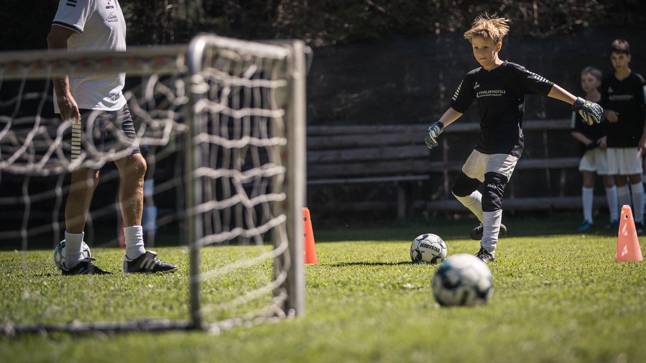 Bambino si allena a calcio con allenatore sull'erba vicino porta e coni