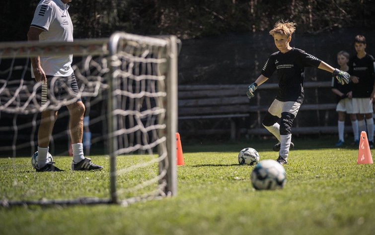 Bambino si allena a calcio con allenatore sull'erba vicino porta e coni