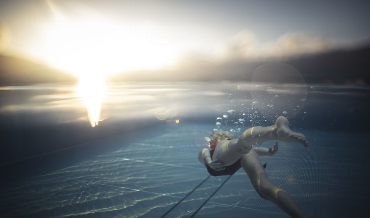 Persona che nuota sott'acqua in piscina al tramonto