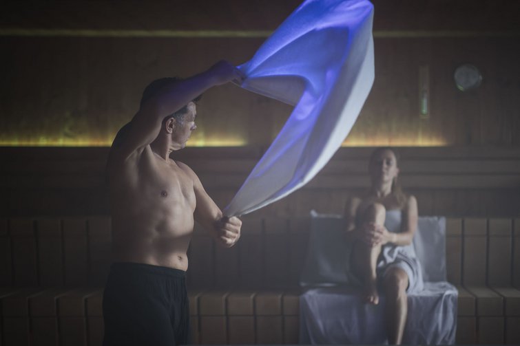 Hotel per yoga in Alto Adige Uomo che agita un asciugamano in sauna, donna rilassata seduta