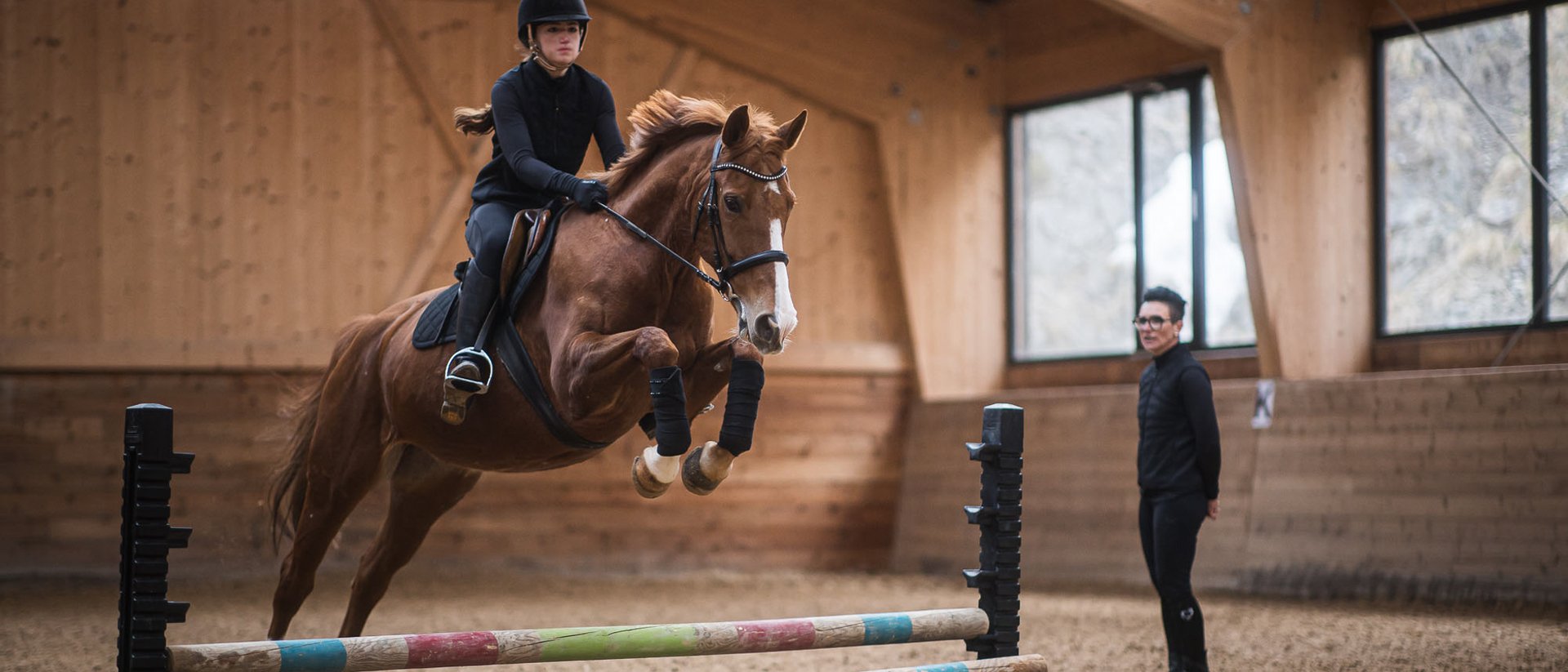Rider jumping horse over obstacle in indoor riding arena