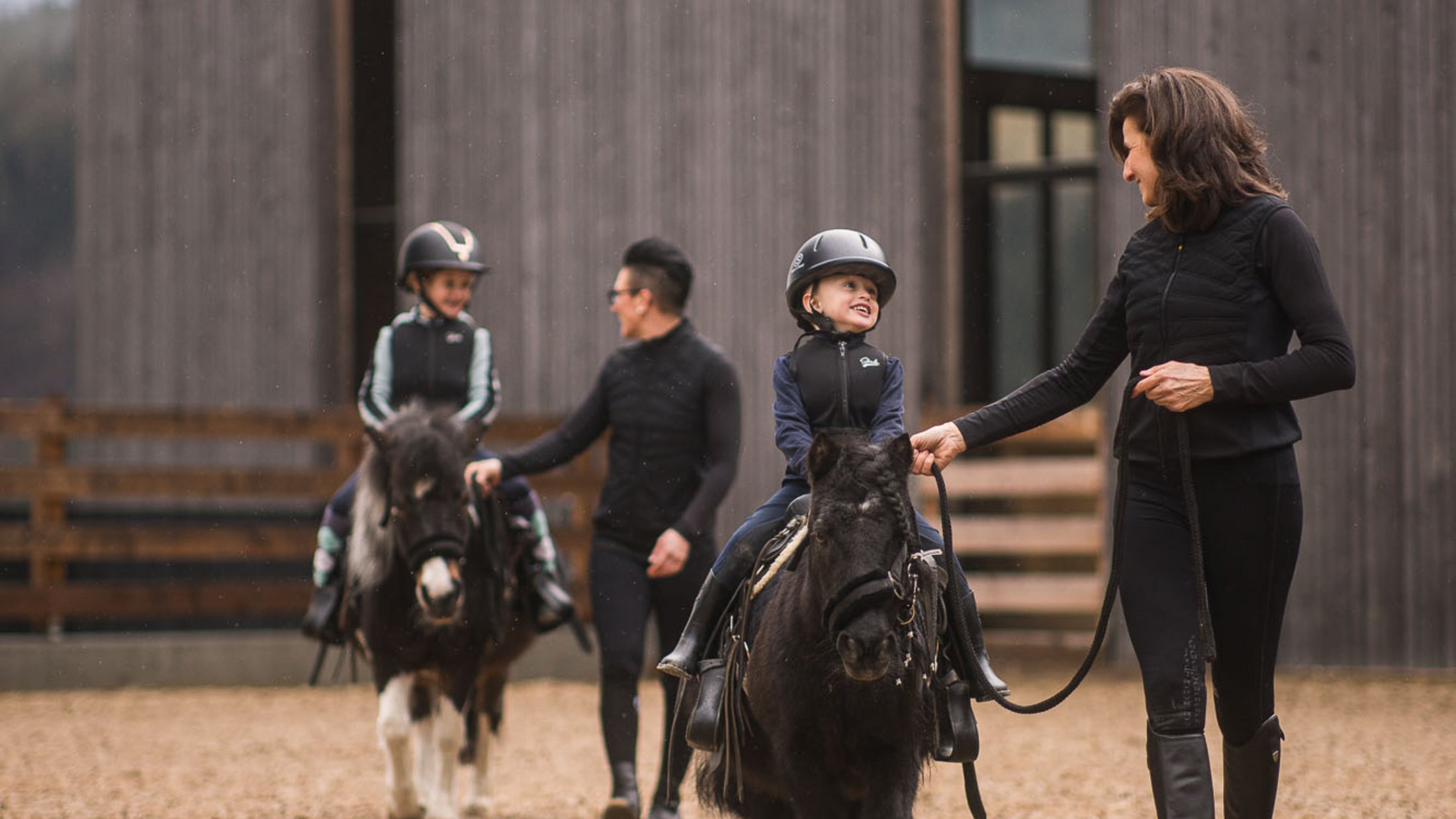 Due bambini cavalcano pony guidati da due adulti in abbigliamento da equitazione