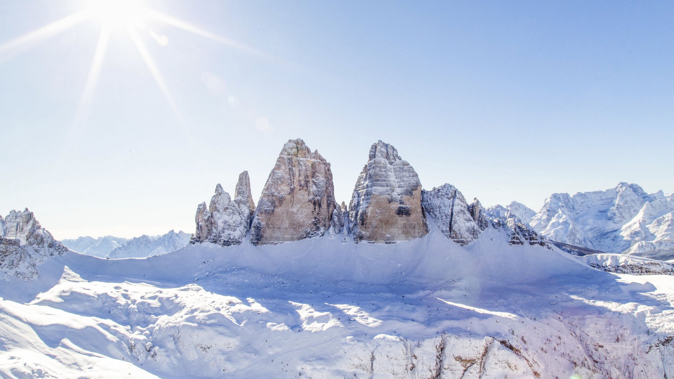 Three snow-covered mountain peaks in bright sunlight