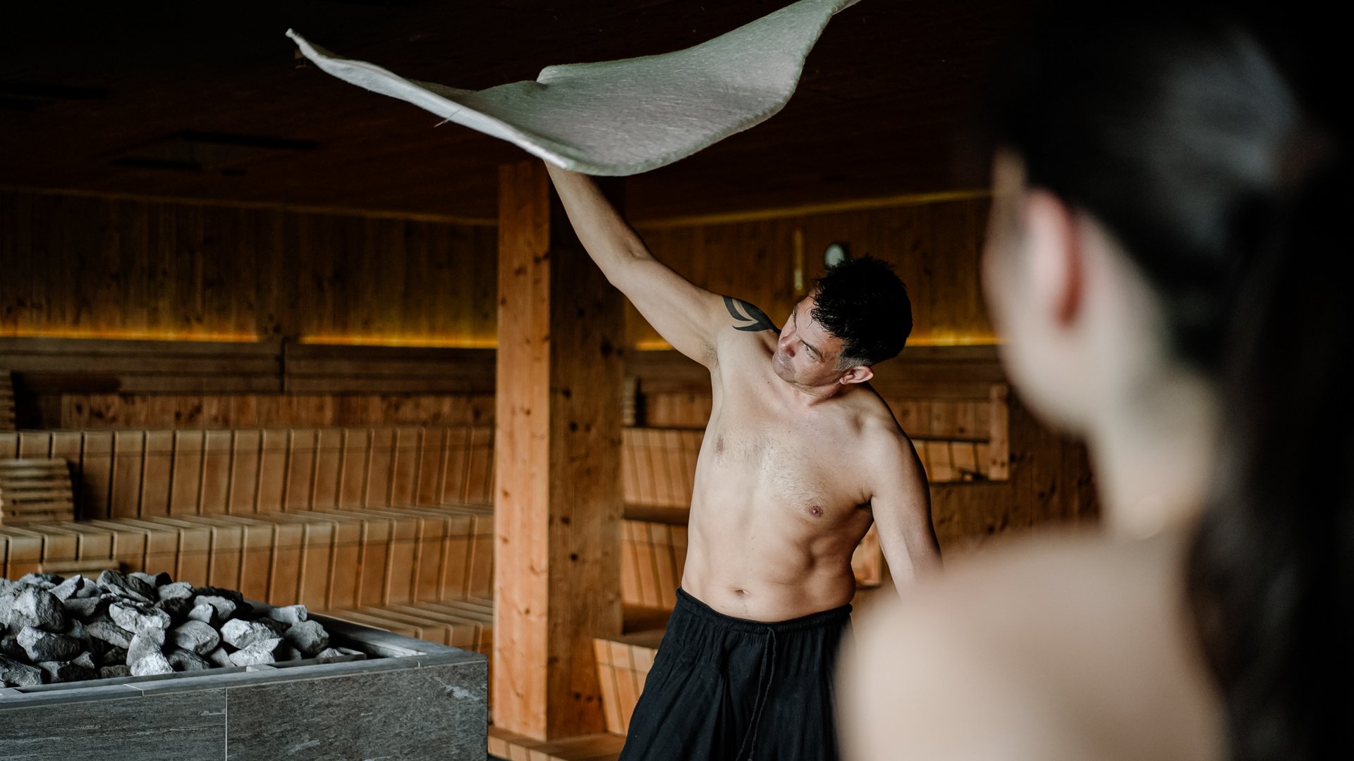 Hotel per yoga in Alto Adige Uomo nella sauna che agita un asciugamano davanti al forno di pietra