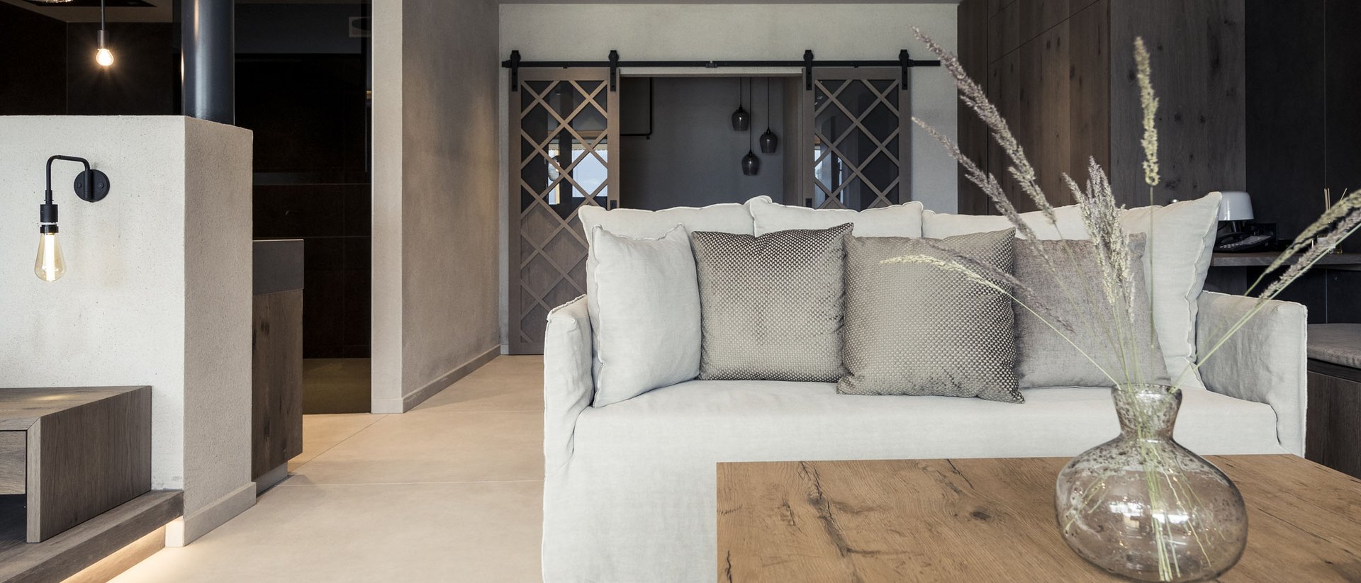 An enriching holiday in your luxury chalet in South Tyrol Modern living room with light gray sofa, wooden table, and decorative vase