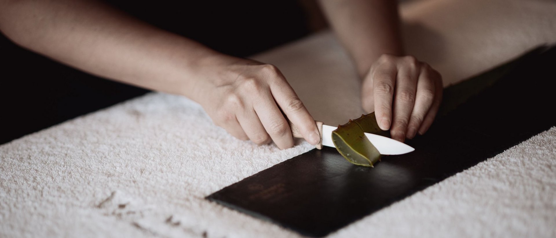 Mani che tagliano una foglia di aloe vera su una superficie nera