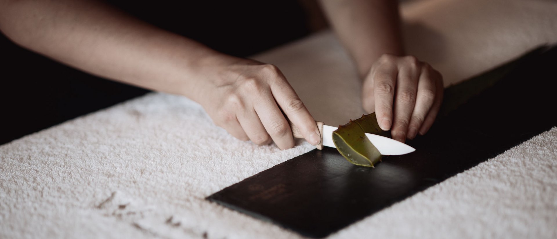 Hände schneiden Aloe Vera Blatt auf schwarzer Unterlage