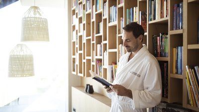 Uomo con accappatoio che legge un libro in una biblioteca moderna con scaffali in legno
