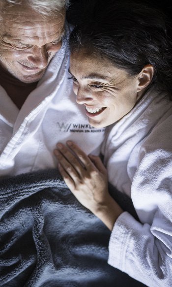 Coppia felice in accappatoi bianchi coccolandosi sotto una coperta