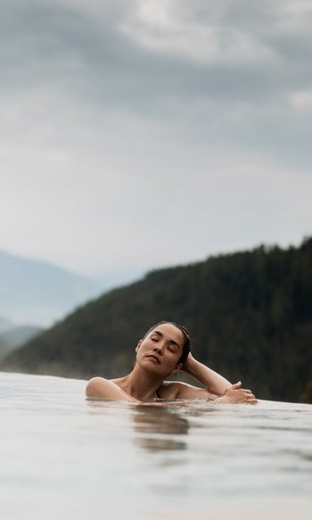 Frau entspannt in Infinity-Pool mit Bergblick und bewölktem Himmel
