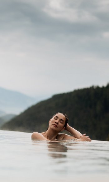 Donna rilassata in piscina a sfioro con vista sulle montagne e cielo nuvoloso