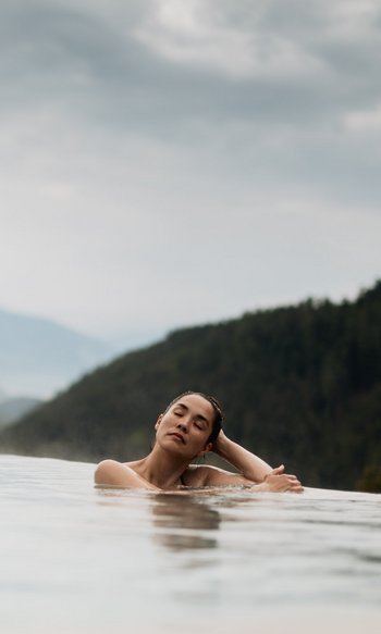 Woman relaxing in infinity pool with mountain views and cloudy sky