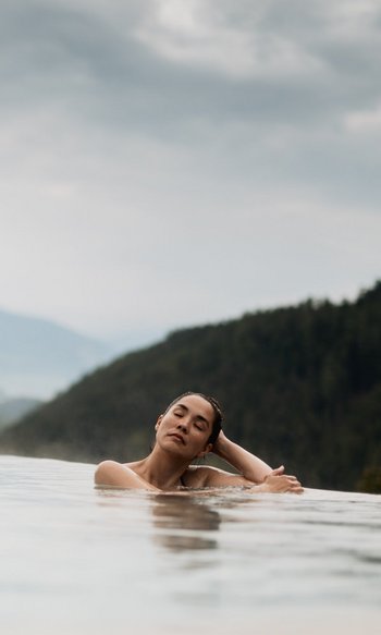 Woman relaxing in infinity pool with mountain views and cloudy sky