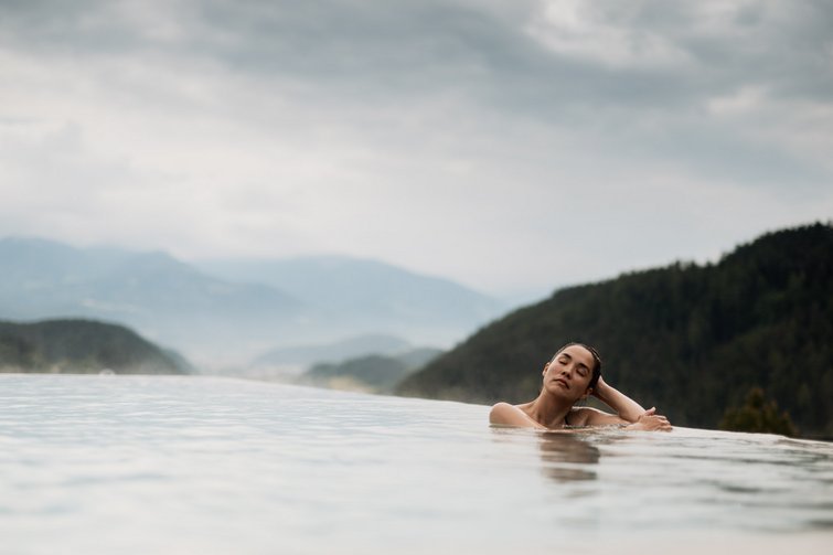 Frau entspannt in Infinity-Pool mit Bergblick und bewölktem Himmel
