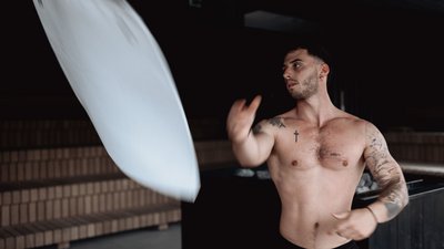Shirtless man quickly throws a pillow indoors with dark background