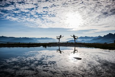 Due persone fanno yoga in montagna con riflesso nell'acqua al tramonto