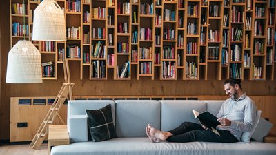 Uomo legge un libro sul divano davanti a una libreria accogliente