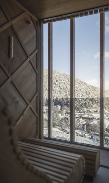 Schnee bedecktes Dorf und Berg vom Fenster einer Holzhütte aus gesehen