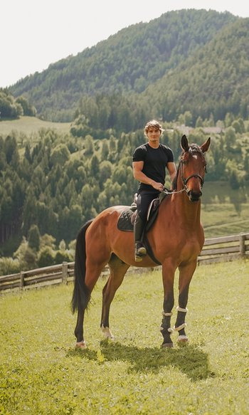 Man riding a brown horse on a meadow with mountains in the background