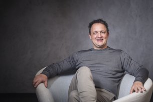 Smiling man in gray sweater sitting relaxed in a chair against dark background