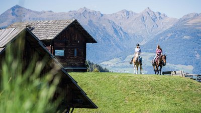 Due persone a cavallo davanti a case di legno e montagne
