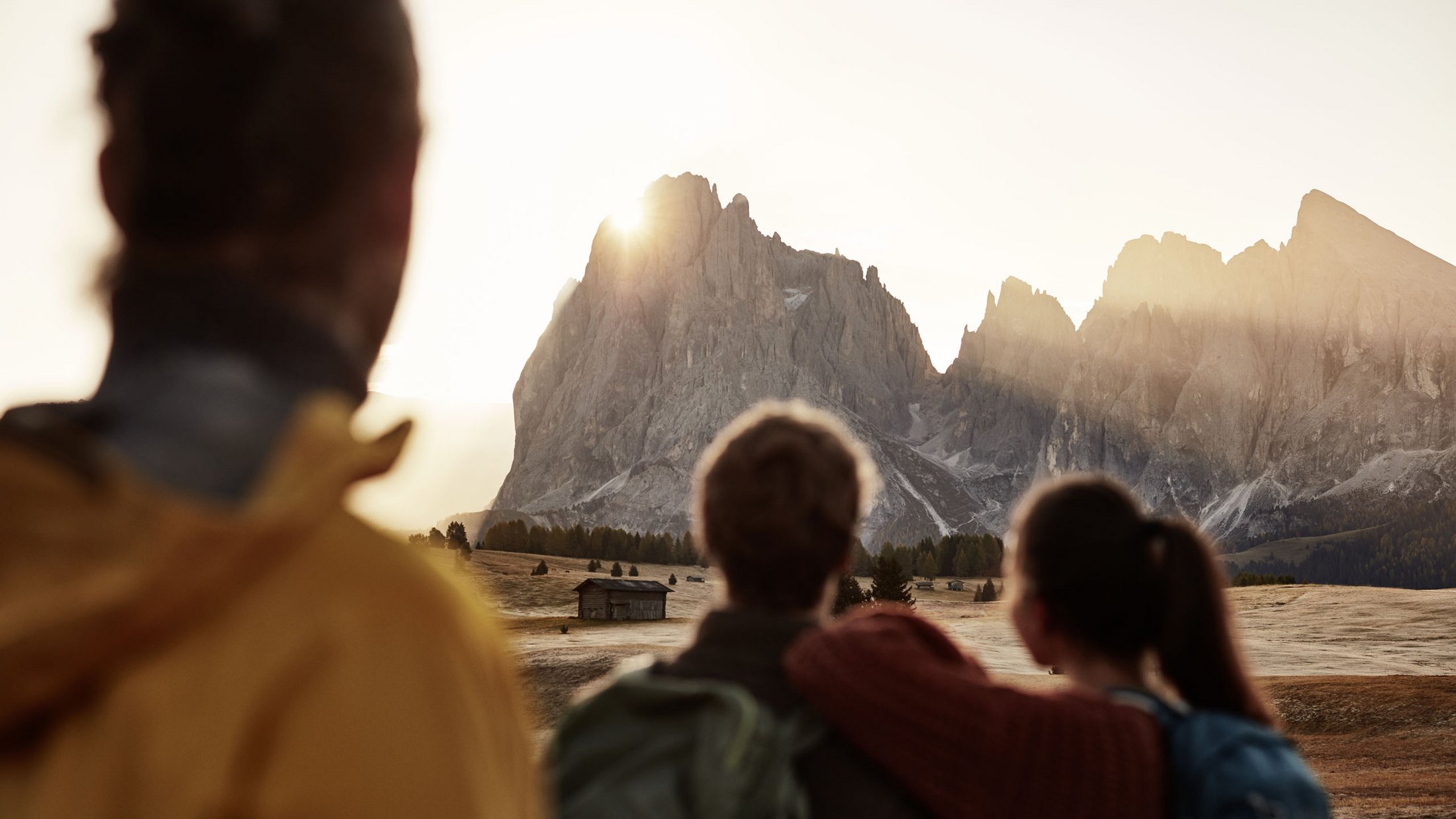 Tre escursionisti guardano il tramonto sulle montagne con una baita