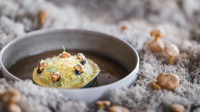 Ravioli finemente impiattati in una ciotola grigia su muschio con piccoli funghi