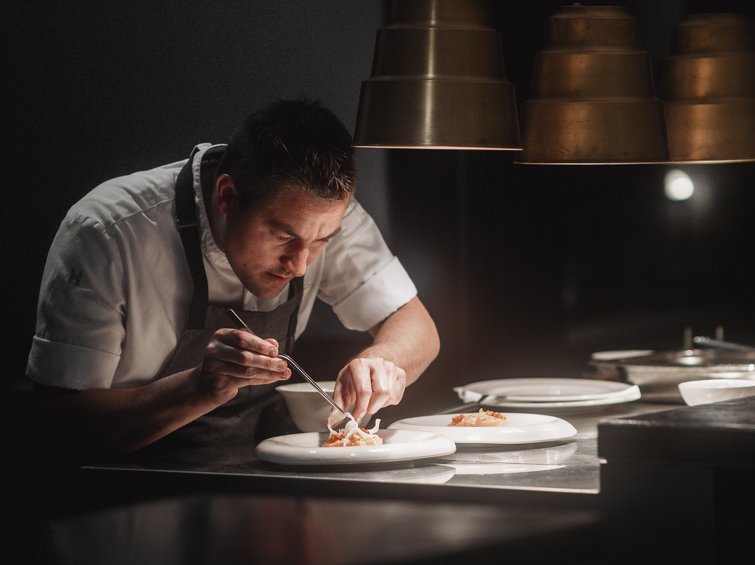 Cuoco che sistema il cibo nei piatti in una cucina professionale con luce soffusa