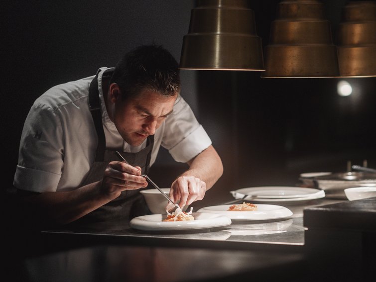 Chef plating food on dishes in a professional kitchen under dim lighting