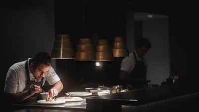 L’esclusività in foto: il nostro chalet in Alto Adige di lusso Cuoco che sistema il cibo nei piatti in una cucina professionale con luce soffusa