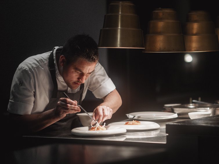 Koch richtet Essen auf Tellern in einer professionellen Küche bei gedämpftem Licht an