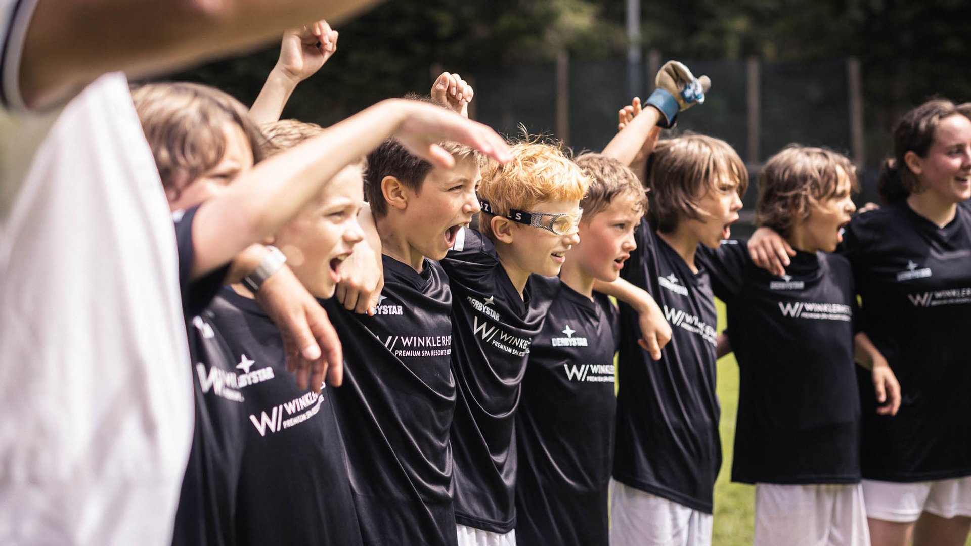 Junge Fußballmannschaft steht Arm in Arm und jubelt auf dem Spielfeld