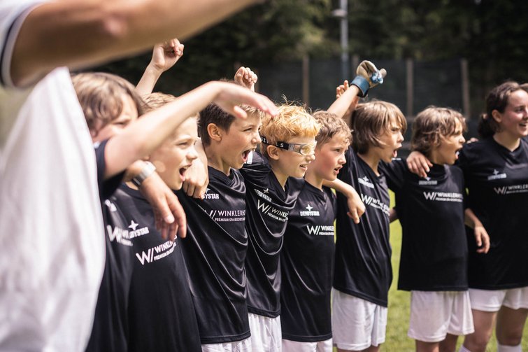 Squadra di giovani calciatori uniti in cerchio che esultano sul campo