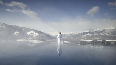 Persona in accappatoio guarda le montagne innevate da una piscina