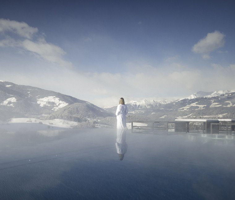 Persona in accappatoio guarda le montagne innevate da una piscina