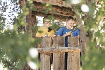 Bambini che guardano oltre una staccionata di legno in un giardino assolato