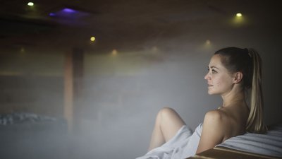 Donna che si rilassa in sauna nebbiosa avvolta in un asciugamano