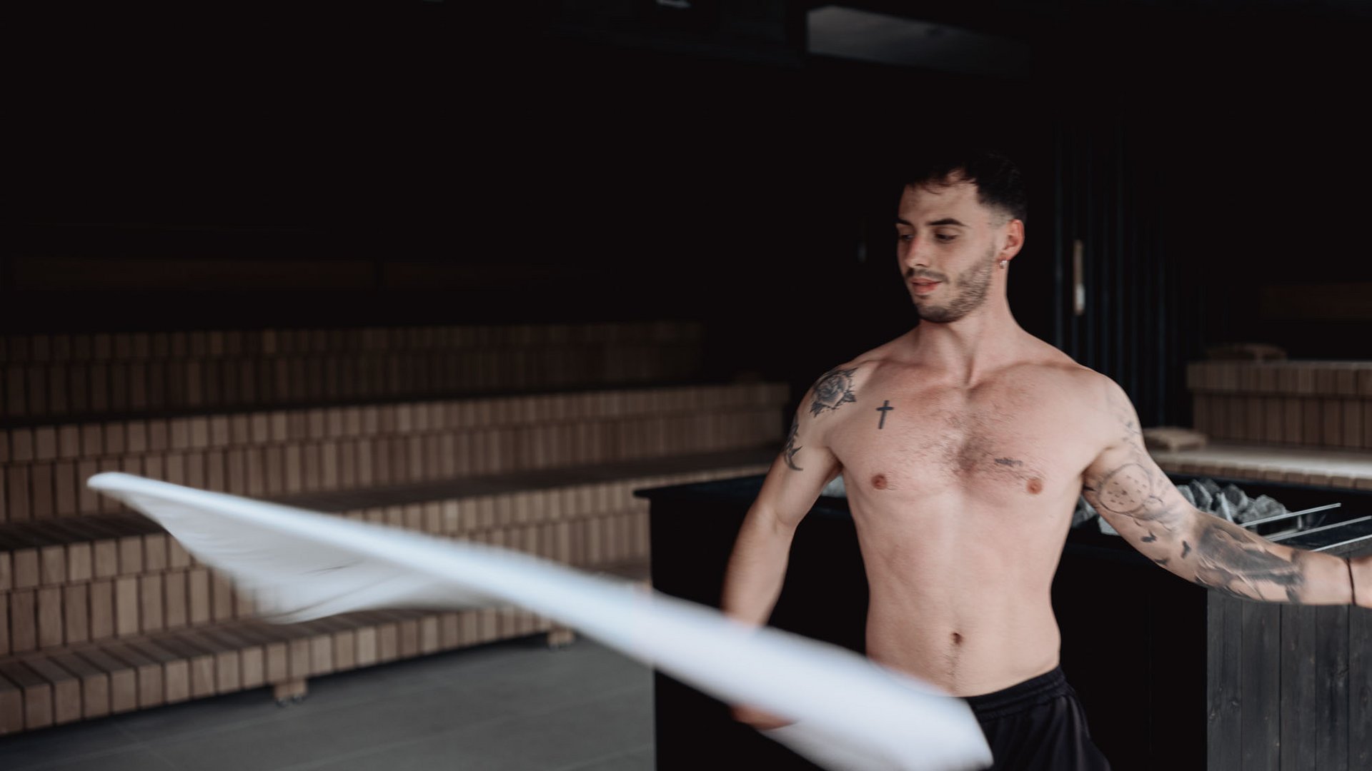 Uomo senza maglietta con tatuaggi agita un panno bianco in una sauna