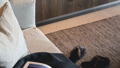 L’esclusività in foto: il nostro chalet in Alto Adige di lusso Rivista aperta su divano davanti a camino moderno e pantofole sul tappeto