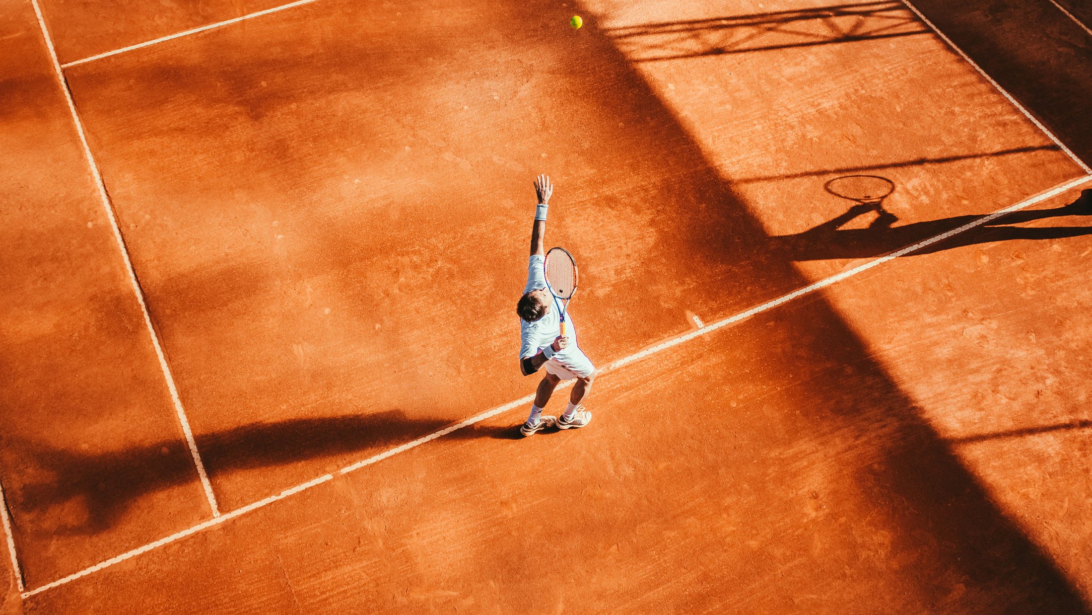 Tennisspieler wirft Ball beim Aufschlag auf Sandplatz