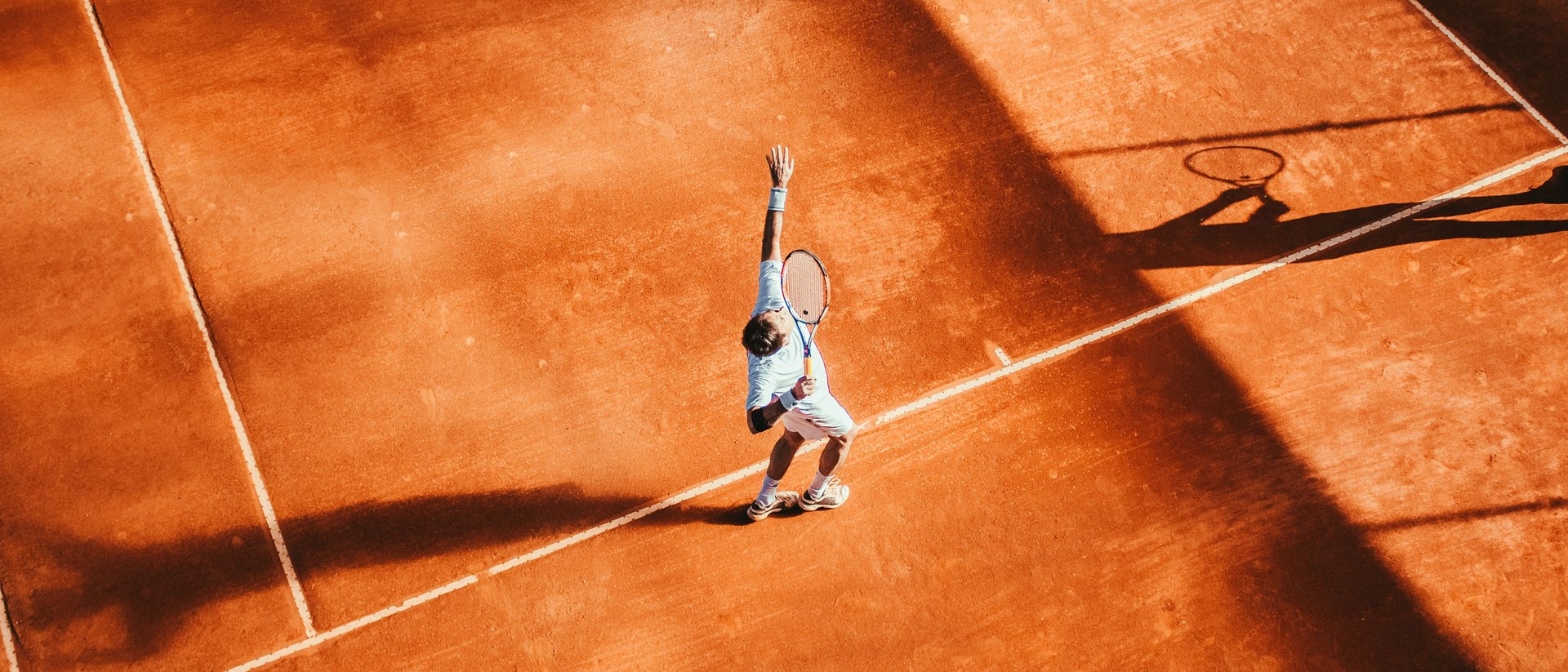Tennis- & Padelurlaub in Südtirol: unser Premium-Service Tennisspieler wirft Ball beim Aufschlag auf Sandplatz