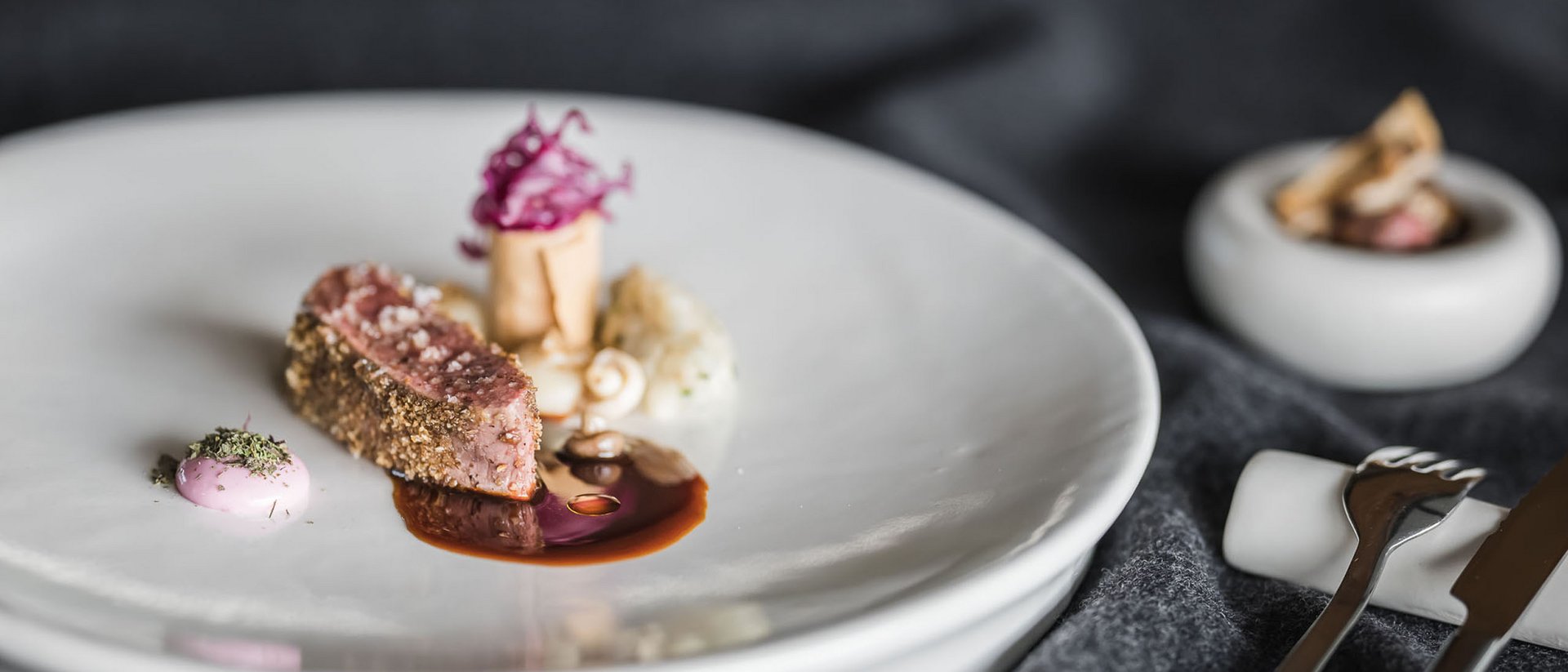 Fein angerichtetes Gourmetgericht mit Fleisch und Soße auf weißem Teller