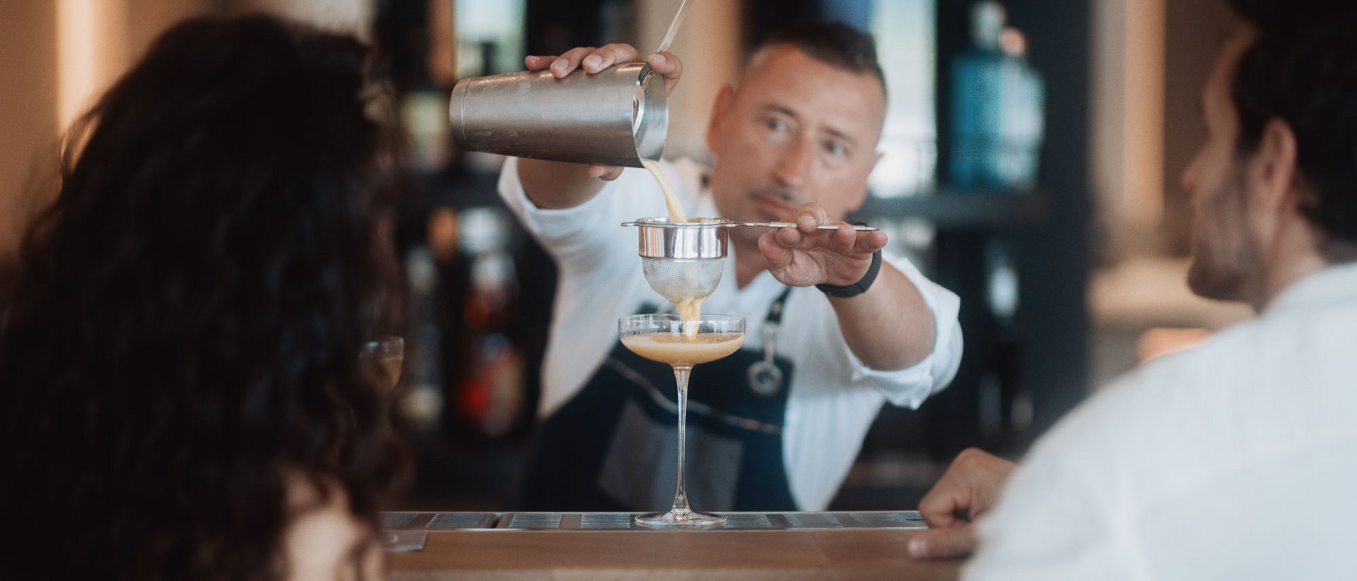 Barkeeper siebt Cocktail für zwei Gäste an der Bar