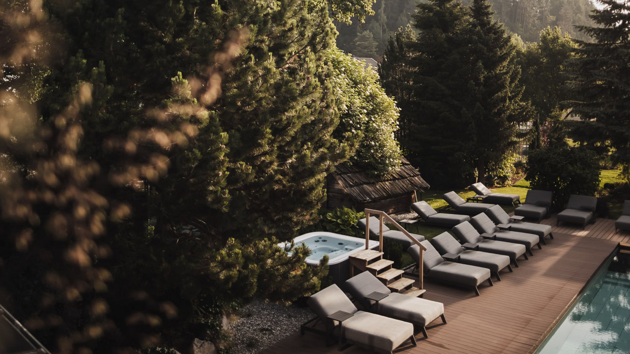 Area piscina con lettini e vasca idromassaggio in paesaggio montano boscoso