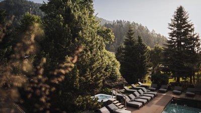 The best photos from our hotel in South Tyrol that kids love Pool area with lounge chairs and hot tub in wooded mountain landscape