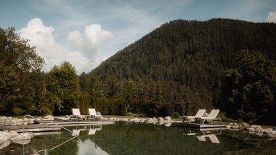 L’esclusività in foto: il nostro chalet in Alto Adige di lusso Piscina naturale con lettini vicino a montagna alberata e cielo azzurro