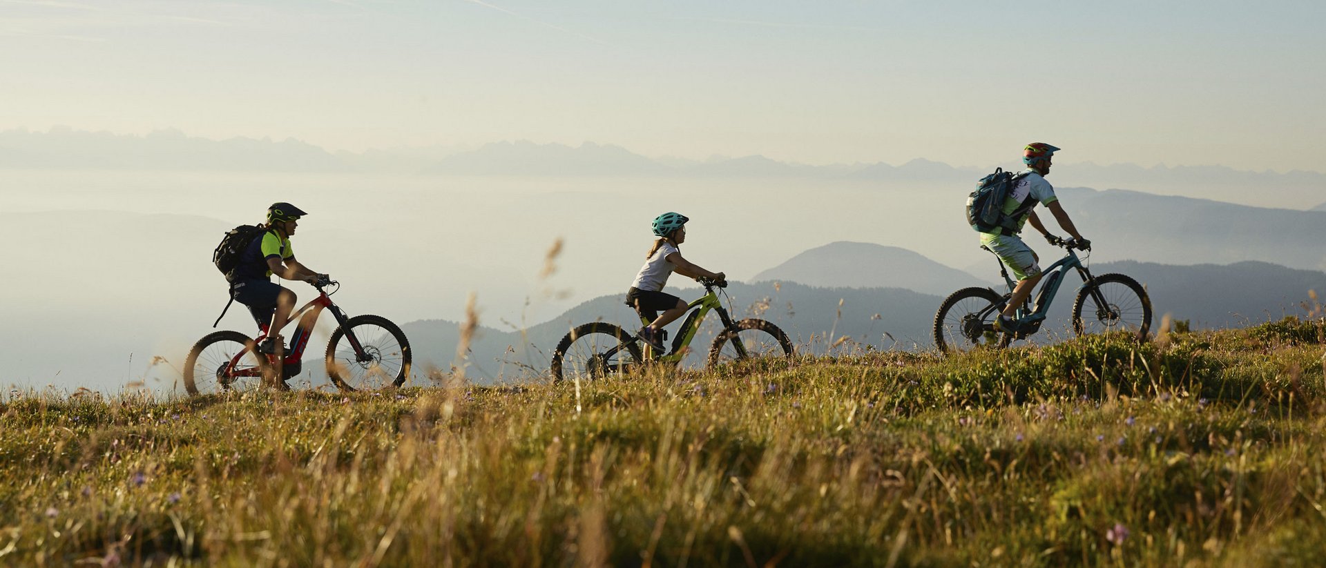 Drei Radfahrer fahren auf einem Berg mit Panoramablick und Gras im Vordergrund