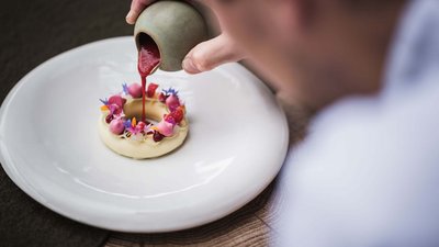 Mano versa salsa rossa su dessert decorato artisticamente su piatto bianco